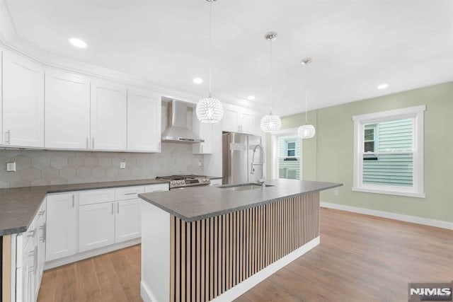 kitchen with a kitchen island with sink, sink, wall chimney range hood, decorative light fixtures, and white cabinetry