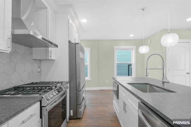 kitchen featuring pendant lighting, appliances with stainless steel finishes, wall chimney exhaust hood, backsplash, and white cabinetry