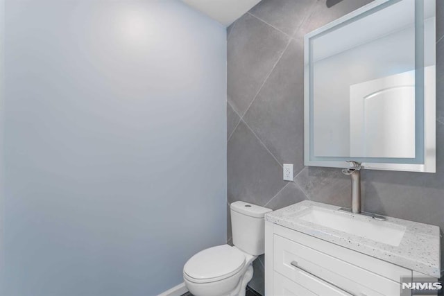 bathroom with vanity, toilet, and tile walls