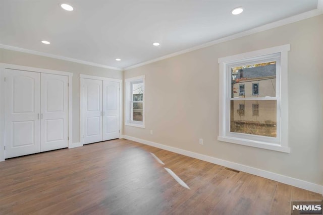 unfurnished bedroom with wood-type flooring, two closets, and ornamental molding