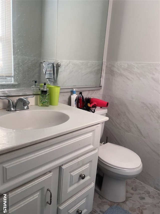 bathroom featuring tile patterned flooring, vanity, toilet, and tile walls