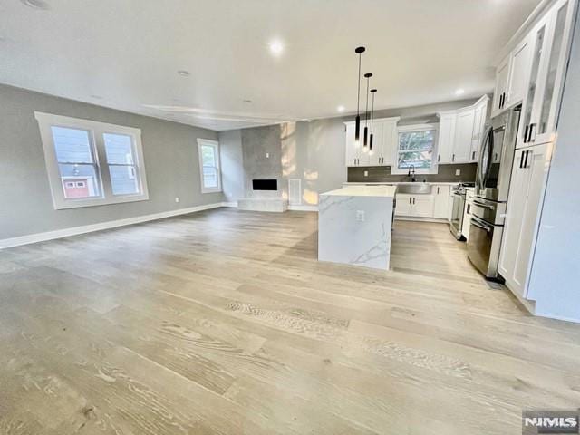 kitchen with a large fireplace, stainless steel appliances, a kitchen island, white cabinetry, and hanging light fixtures