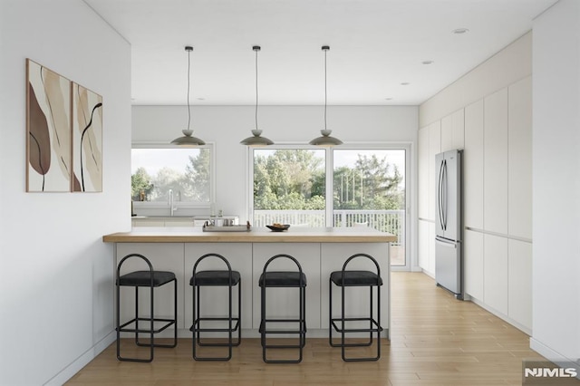 kitchen featuring a breakfast bar area, stainless steel refrigerator, white cabinetry, and decorative light fixtures