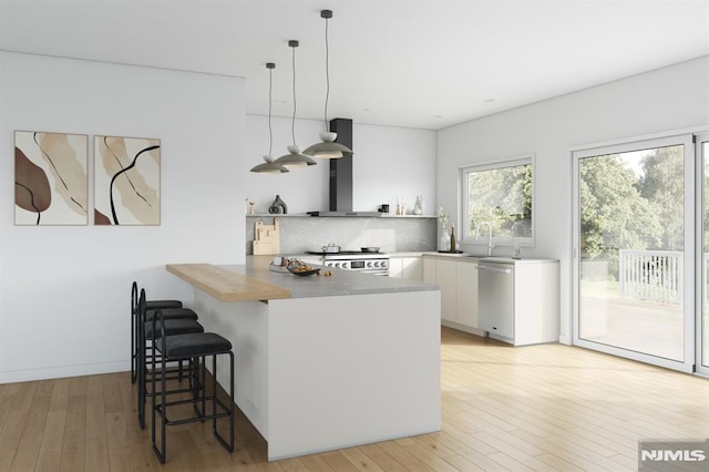 kitchen featuring kitchen peninsula, appliances with stainless steel finishes, wall chimney exhaust hood, decorative light fixtures, and white cabinetry