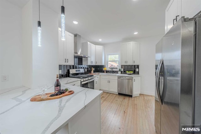 kitchen with light stone countertops, wall chimney exhaust hood, stainless steel appliances, pendant lighting, and white cabinets