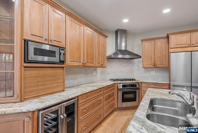 kitchen featuring backsplash, appliances with stainless steel finishes, a sink, wall chimney range hood, and beverage cooler