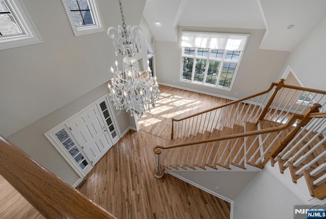 stairs featuring wood finished floors, a towering ceiling, baseboards, and an inviting chandelier