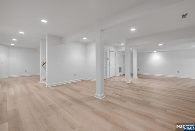 finished basement featuring recessed lighting, visible vents, light wood-style flooring, and stairs