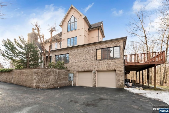 exterior space with brick siding, aphalt driveway, an attached garage, a wooden deck, and stucco siding