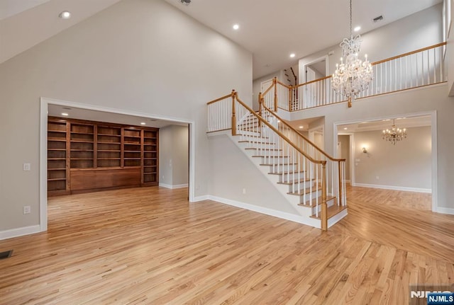 unfurnished living room featuring a high ceiling, an inviting chandelier, wood finished floors, baseboards, and stairs