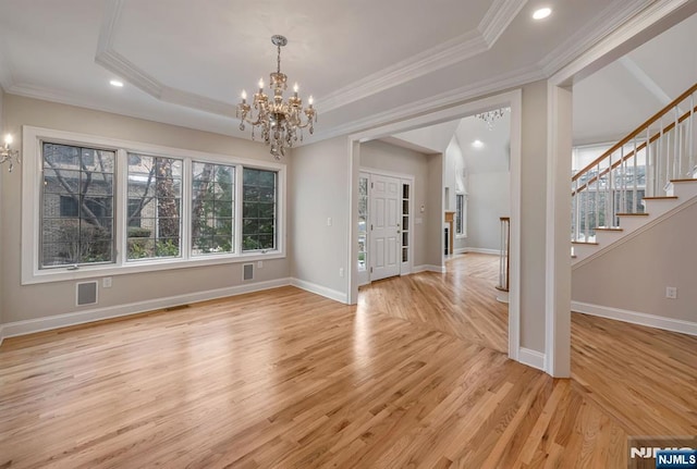 unfurnished dining area with a chandelier, ornamental molding, stairway, light wood-type flooring, and a tray ceiling