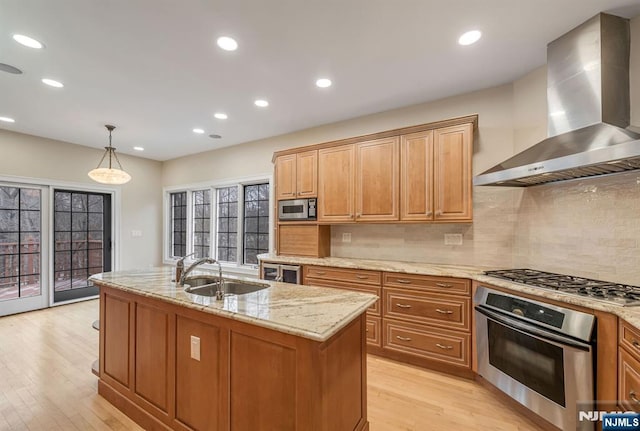 kitchen featuring stainless steel appliances, light wood-style floors, a sink, and wall chimney exhaust hood