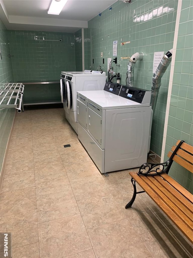 laundry area with light tile patterned flooring, washer and dryer, and tile walls