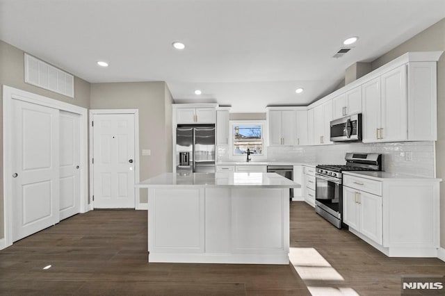 kitchen featuring a center island, dark wood-type flooring, white cabinets, decorative backsplash, and appliances with stainless steel finishes