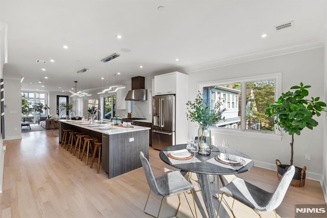 kitchen featuring high end refrigerator, white cabinets, a center island with sink, ornamental molding, and decorative light fixtures