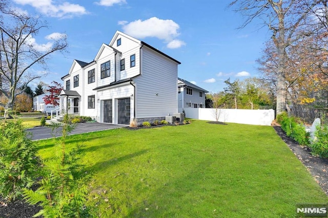 back of house with central air condition unit, a garage, and a lawn