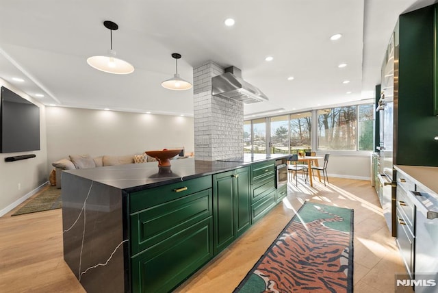 kitchen with light wood-type flooring, wall chimney exhaust hood, black electric cooktop, green cabinetry, and hanging light fixtures