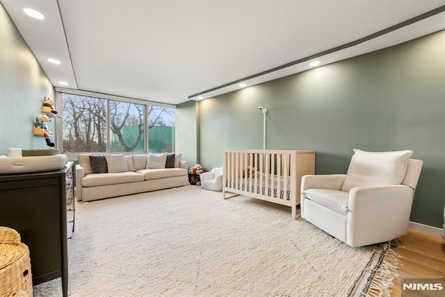 bedroom with hardwood / wood-style flooring, expansive windows, and a nursery area