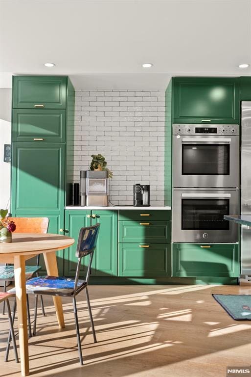 kitchen with double oven, green cabinets, and hardwood / wood-style flooring