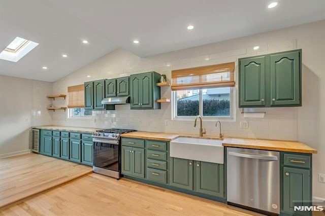 kitchen with sink, green cabinets, wooden counters, vaulted ceiling with skylight, and appliances with stainless steel finishes