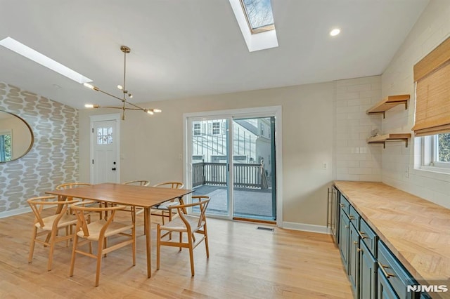 dining space with a notable chandelier, light wood-type flooring, and lofted ceiling with skylight