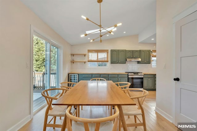 dining space featuring a notable chandelier, light hardwood / wood-style flooring, vaulted ceiling, and beverage cooler