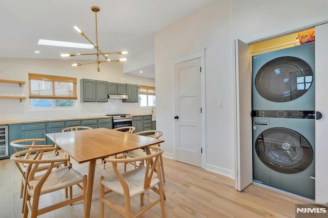 kitchen featuring stainless steel range, stacked washer / drying machine, decorative backsplash, an inviting chandelier, and lofted ceiling