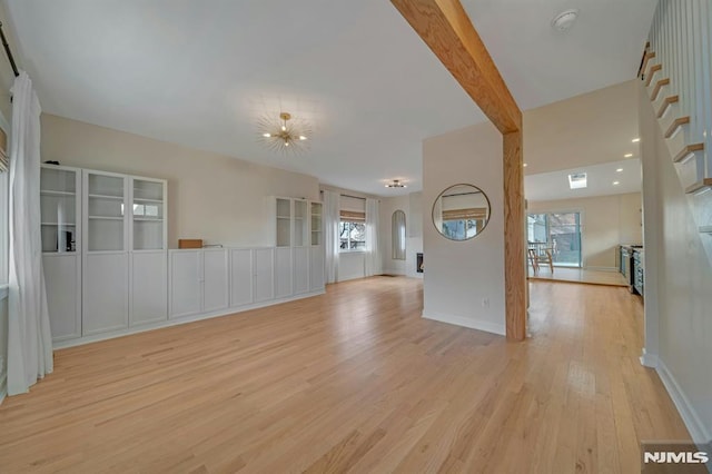 empty room with beam ceiling, a notable chandelier, and light hardwood / wood-style flooring