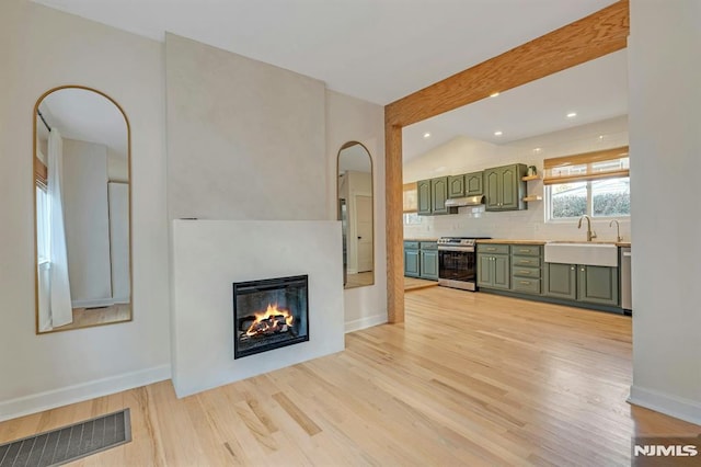 unfurnished living room featuring sink, light wood-type flooring, and lofted ceiling