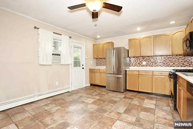 kitchen with light brown cabinetry, stainless steel appliances, a baseboard radiator, and tasteful backsplash