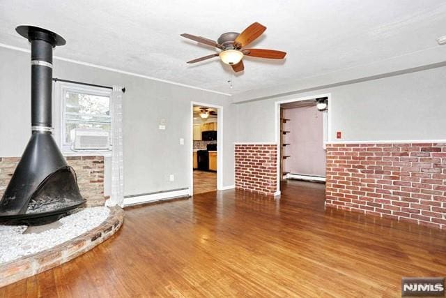 unfurnished living room featuring hardwood / wood-style flooring, a wood stove, baseboard heating, and brick wall