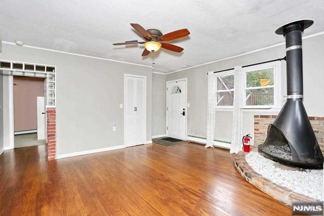 interior space featuring wood-type flooring, a wood stove, ceiling fan, and a baseboard heating unit