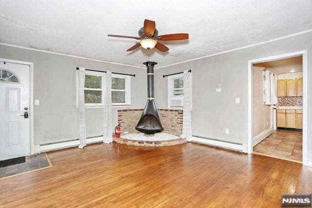 unfurnished living room featuring light hardwood / wood-style floors, a wood stove, ceiling fan, and a baseboard radiator