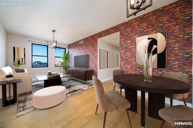 dining room featuring wood-type flooring, brick wall, and an inviting chandelier