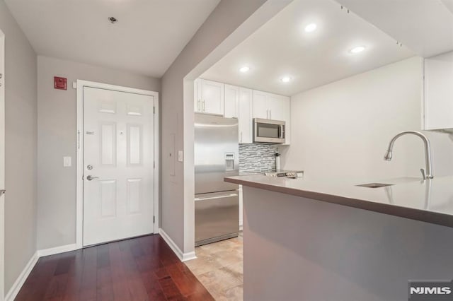 kitchen featuring sink, appliances with stainless steel finishes, tasteful backsplash, white cabinetry, and kitchen peninsula