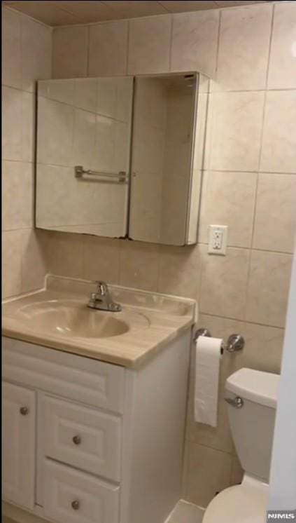 bathroom with vanity, tile walls, and toilet