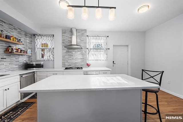 kitchen with wall chimney exhaust hood, hanging light fixtures, decorative backsplash, a breakfast bar, and a kitchen island