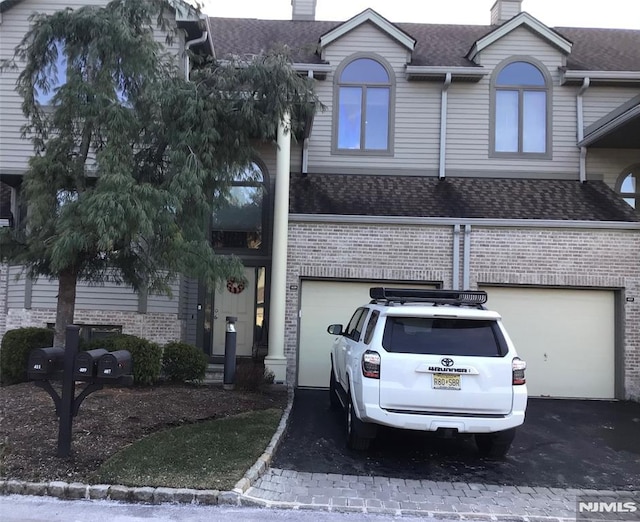 multi unit property featuring driveway, a garage, a chimney, roof with shingles, and brick siding