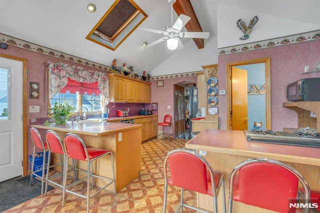 kitchen featuring kitchen peninsula, lofted ceiling with skylight, a breakfast bar area, ceiling fan, and sink