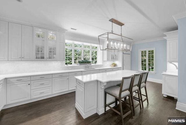 kitchen with a center island, crown molding, hanging light fixtures, white cabinetry, and a breakfast bar area