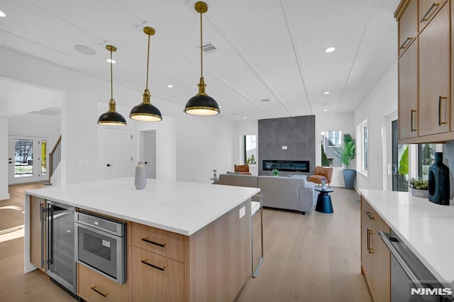 kitchen with light brown cabinetry, decorative light fixtures, a fireplace, a center island, and wine cooler