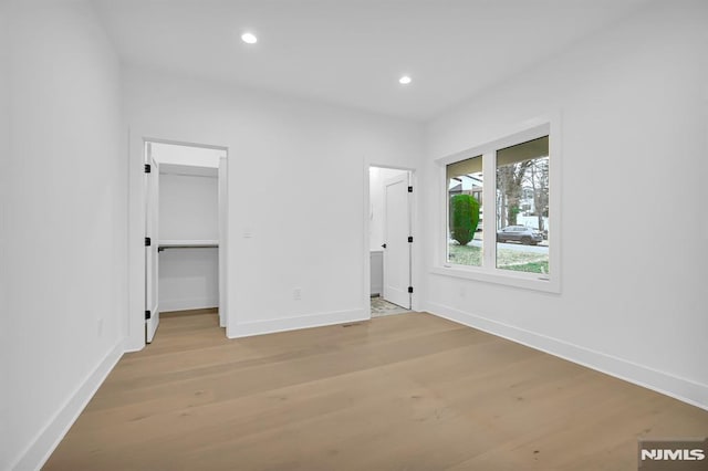 unfurnished bedroom with a closet, a spacious closet, and light hardwood / wood-style flooring