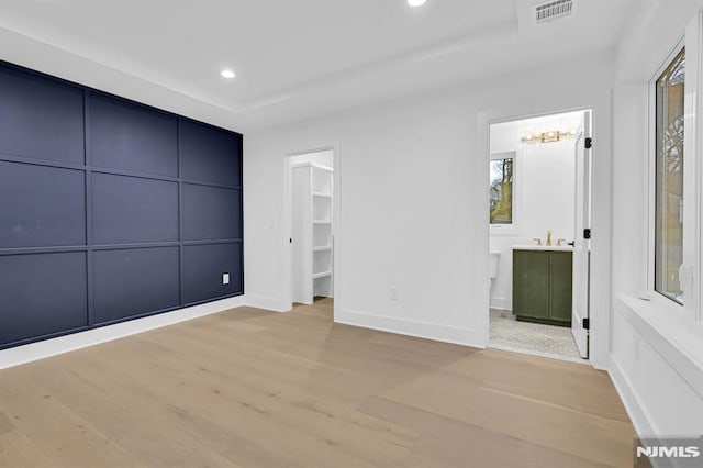 unfurnished bedroom featuring connected bathroom, sink, light hardwood / wood-style floors, a tray ceiling, and a walk in closet