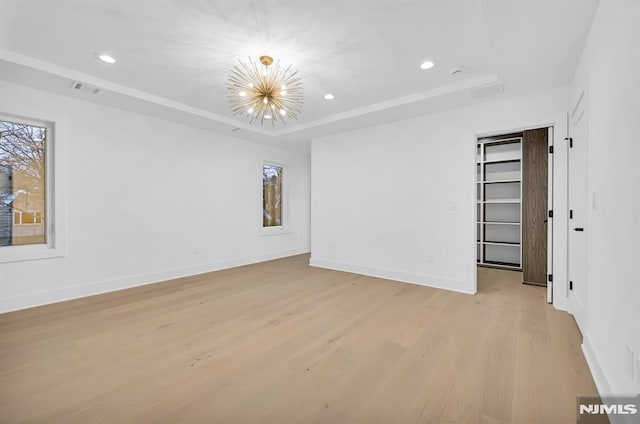 unfurnished room featuring a tray ceiling, an inviting chandelier, and light hardwood / wood-style flooring