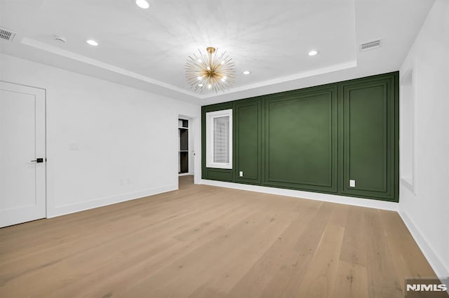 unfurnished room with a raised ceiling, light wood-type flooring, and an inviting chandelier