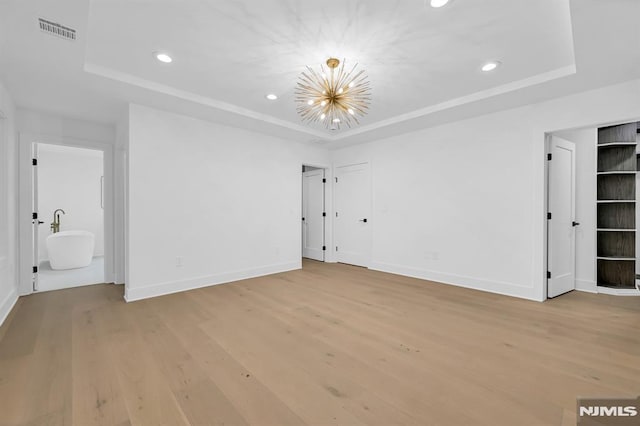 interior space featuring a raised ceiling, ensuite bath, light hardwood / wood-style floors, and an inviting chandelier