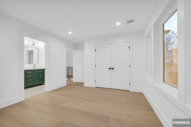 unfurnished bedroom with connected bathroom, a closet, and light hardwood / wood-style flooring