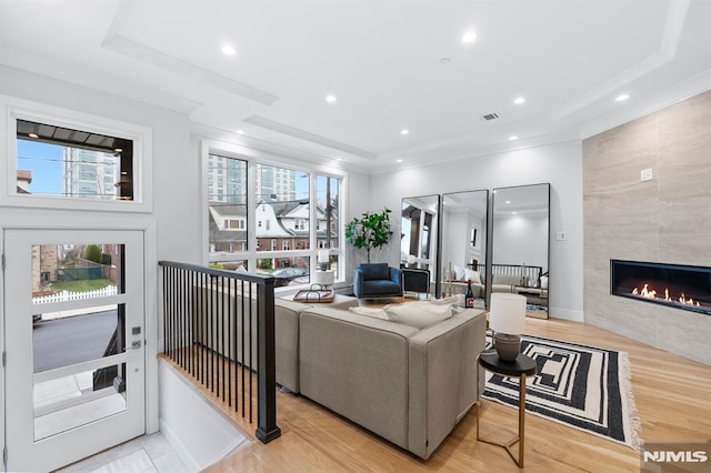 living room featuring a raised ceiling, light wood-type flooring, and a tile fireplace