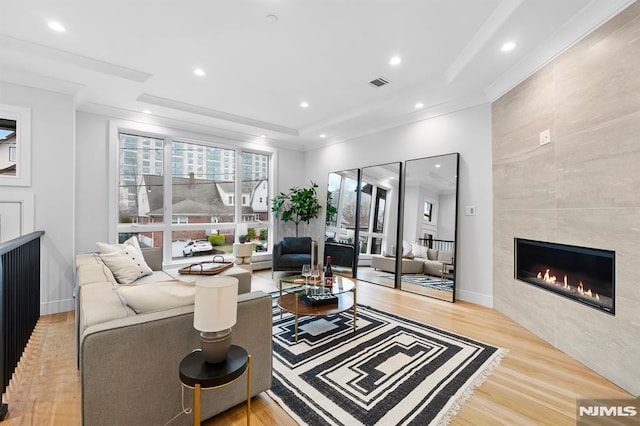 living room with a tray ceiling, a tile fireplace, light hardwood / wood-style floors, and ornamental molding