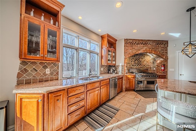 kitchen with light stone countertops, appliances with stainless steel finishes, backsplash, sink, and decorative light fixtures